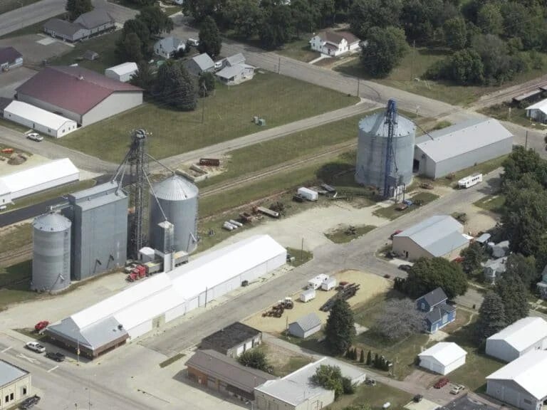 An aerial view of a rural area featuring barns, silos, small houses, and open fields.
