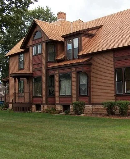 A large Victorian-style house with a gabled roof, multiple windows, and a small front yard with bushes.