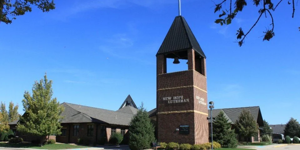 A brick church with a tall steeple, surrounded by trees under a blue sky.