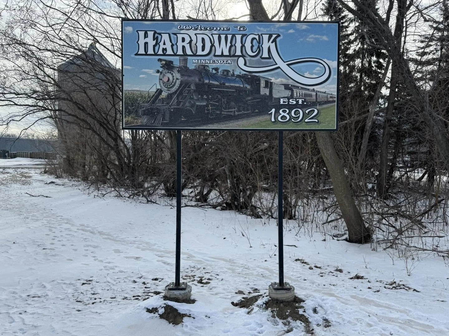 Welcome to Hardwick, Minnesota sign with a historic steam locomotive and train, established 1892, in winter.