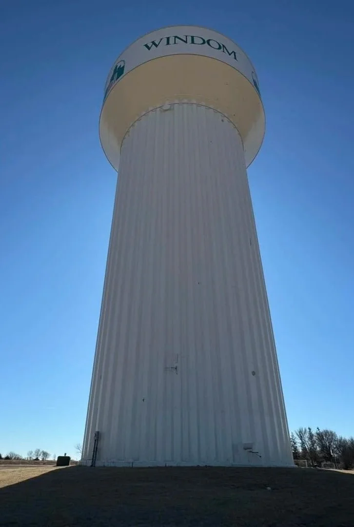 A tall white water tower with the word 'WINDOM' on top, set against a clear blue sky.