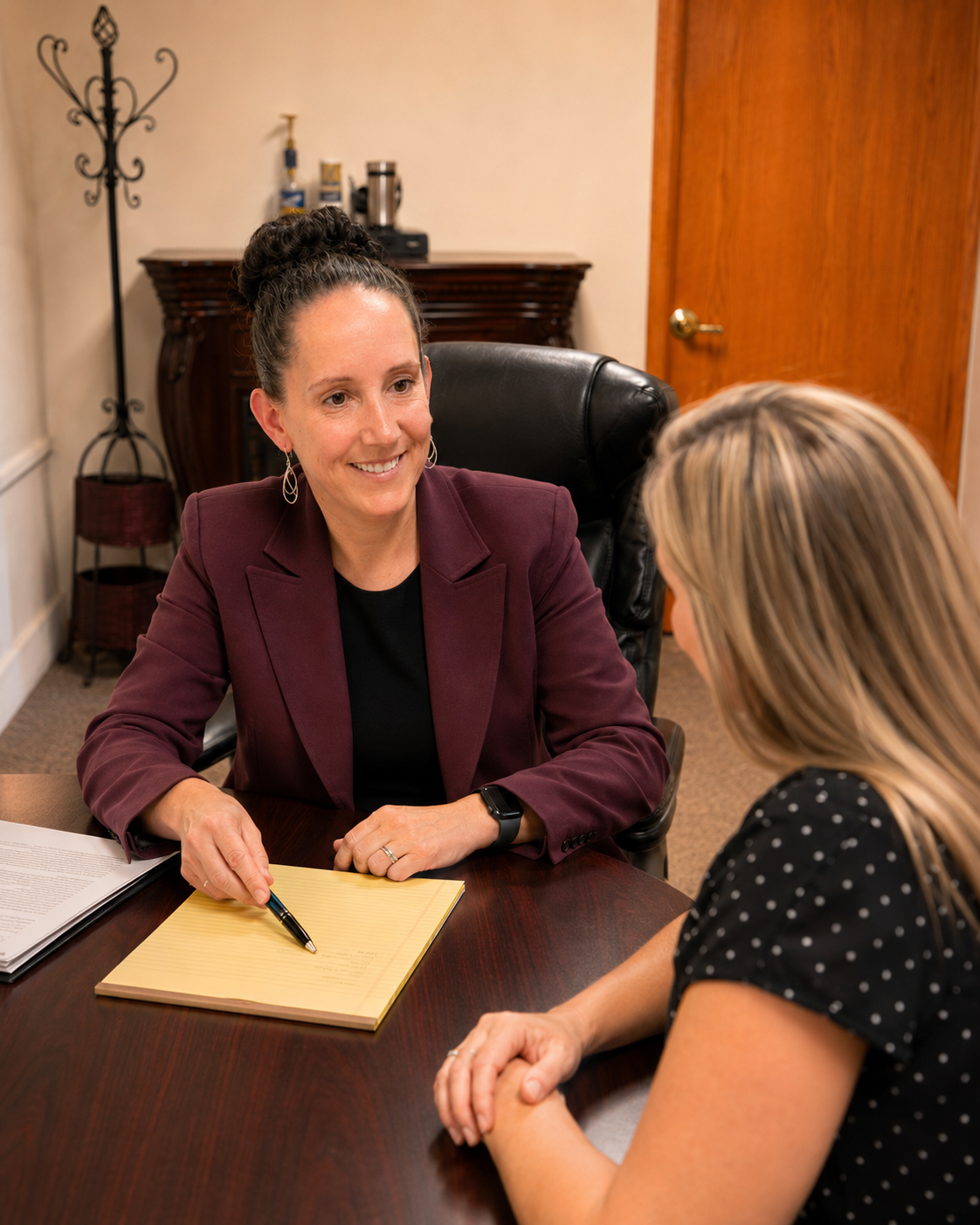 Ginny and a client are having a conversation in Ginny's office, one is smiling and pointing at a yellow notepad on the desk.