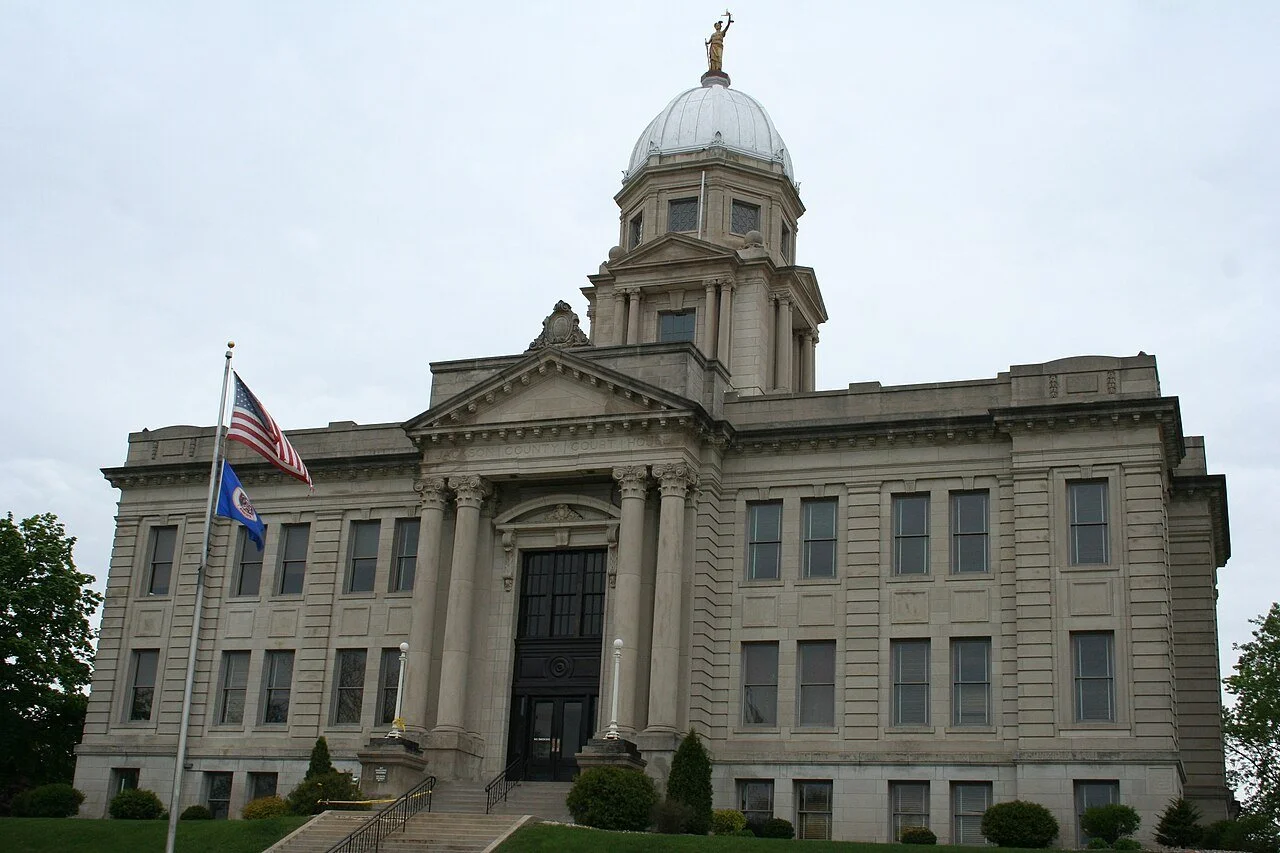 State capitol building with flags and overcast sky.