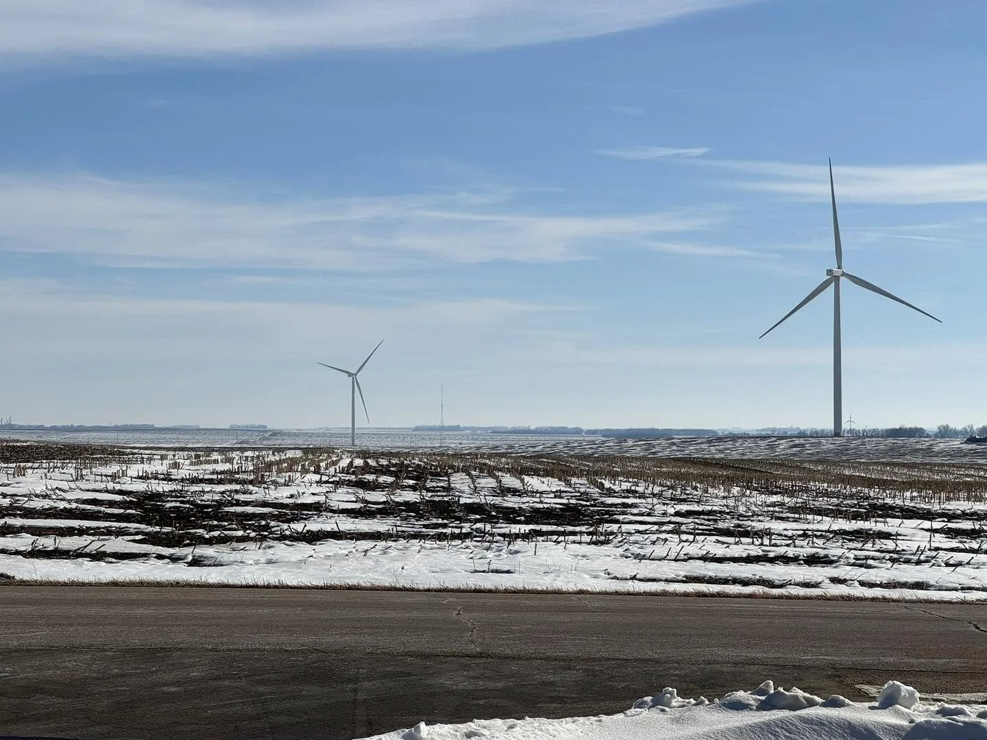 Snow-covered agricultural field with wind turbines and a clear blue sky.