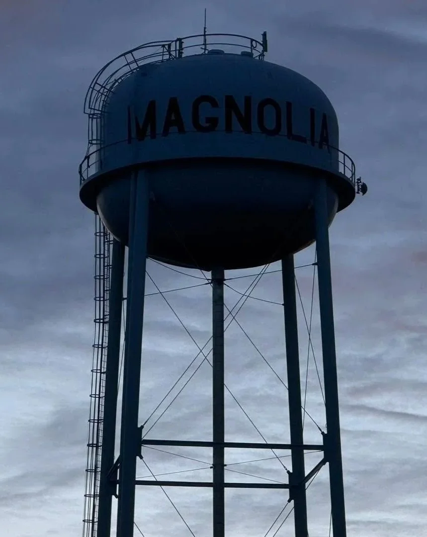 A tall, blue water tower with the word magnolia painted on it, set against a cloudy sky.