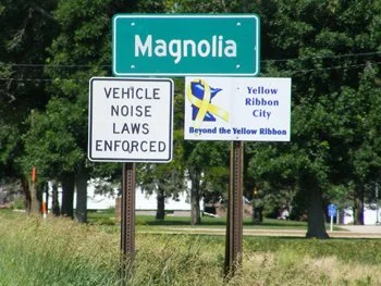 Green road sign reading Magnaolia with additional signs below indicating vehicle noise laws and a Yellow Ribbon City sign.