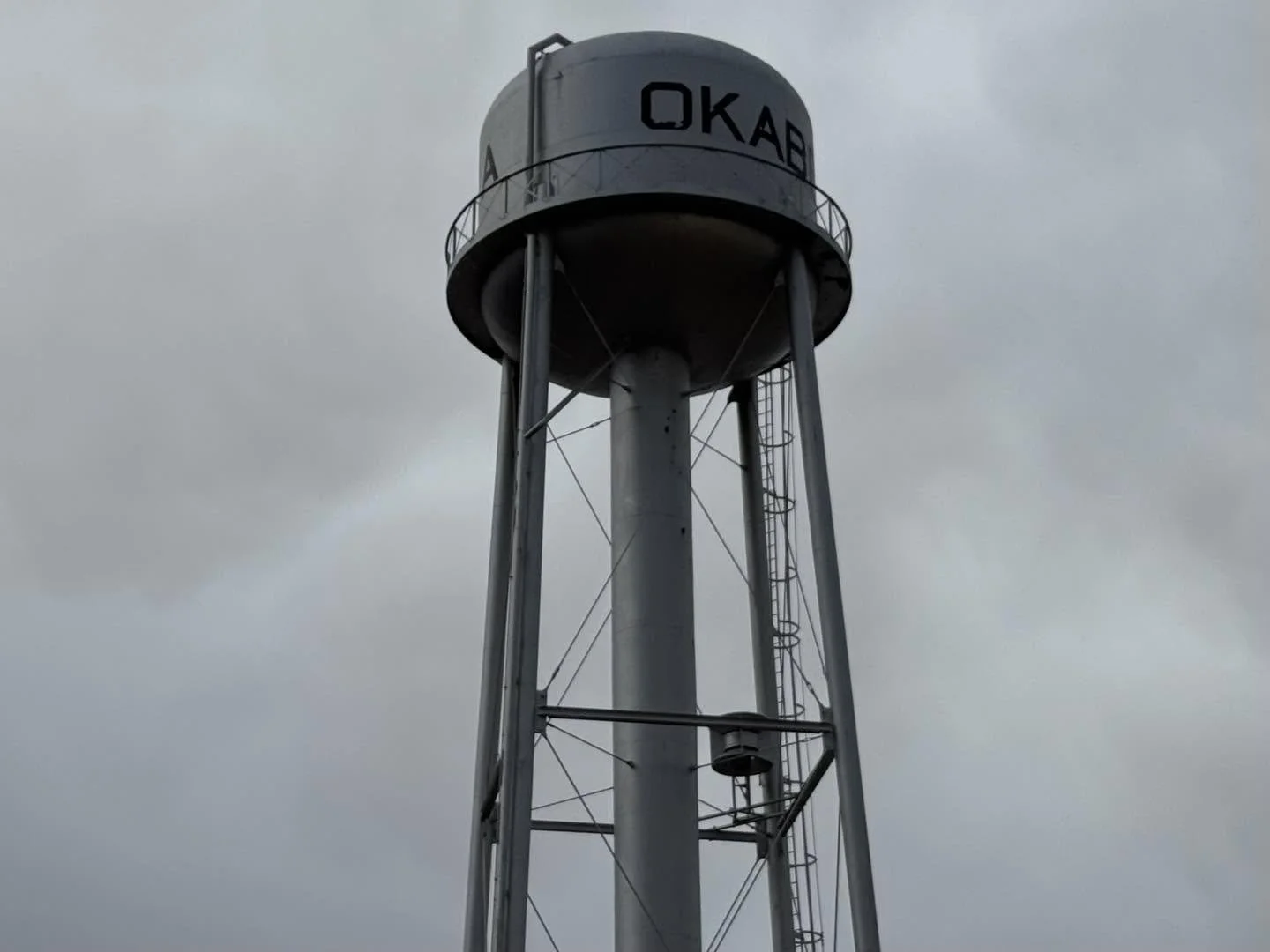 A tall water tower painted in light gray with the word OKAB on it, under a cloudy sky.