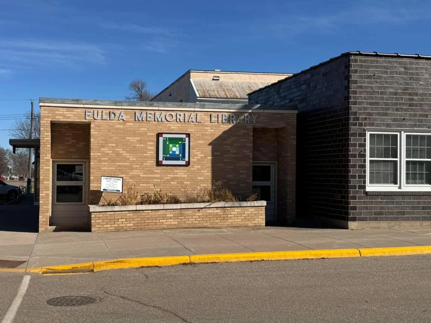 Exterior of Fulda Memorial Library building with brick construction, library sign, and a colorful tile artwork on the wall.