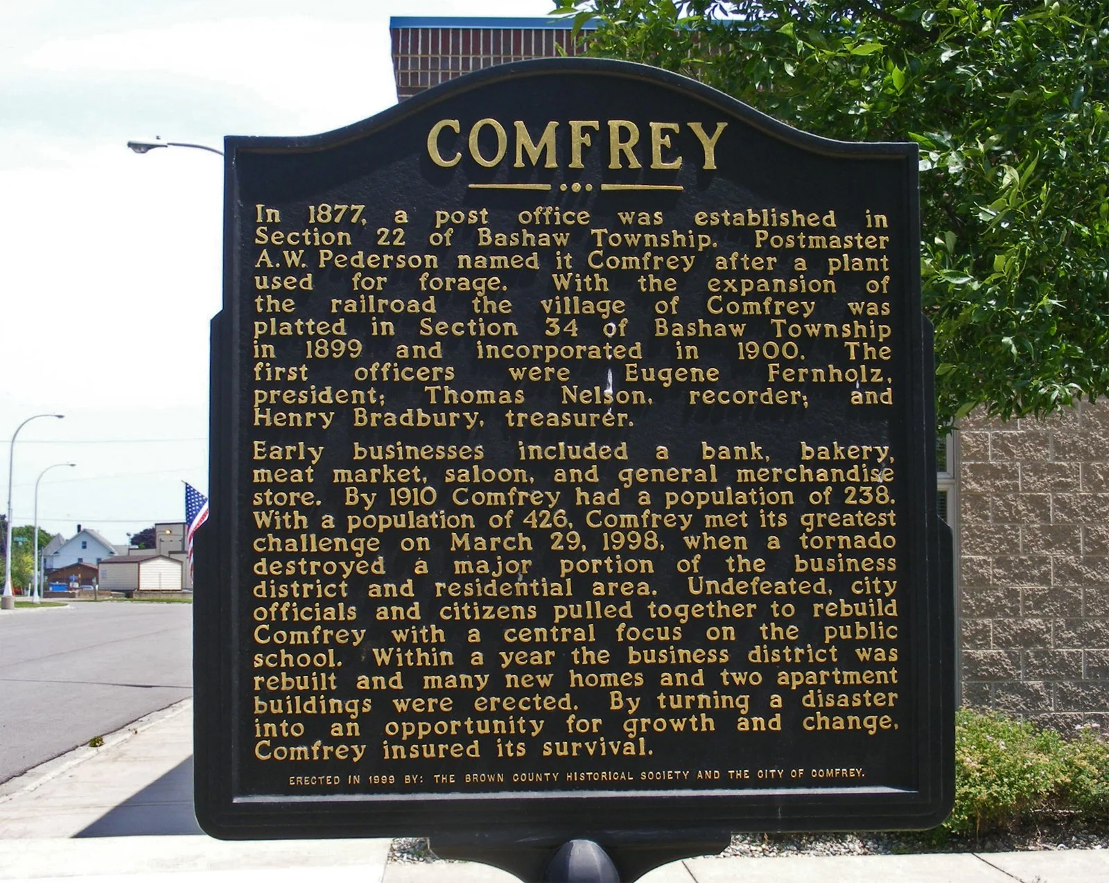 Historical marker depicting the history of Comfrey, established in 1877, with details about its development, early businesses, population growth, and significant challenges including a tornado in 1998.