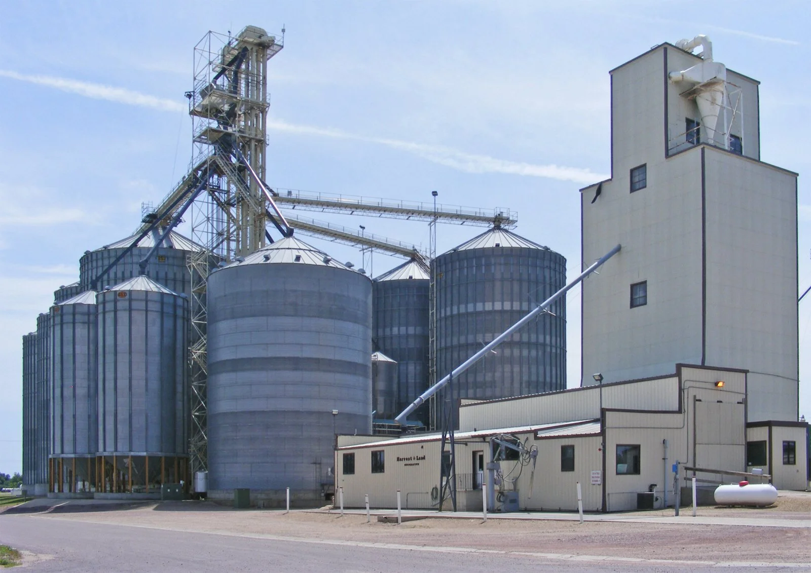 An industrial grain elevator with multiple silos and storage buildings under a partly cloudy sky.