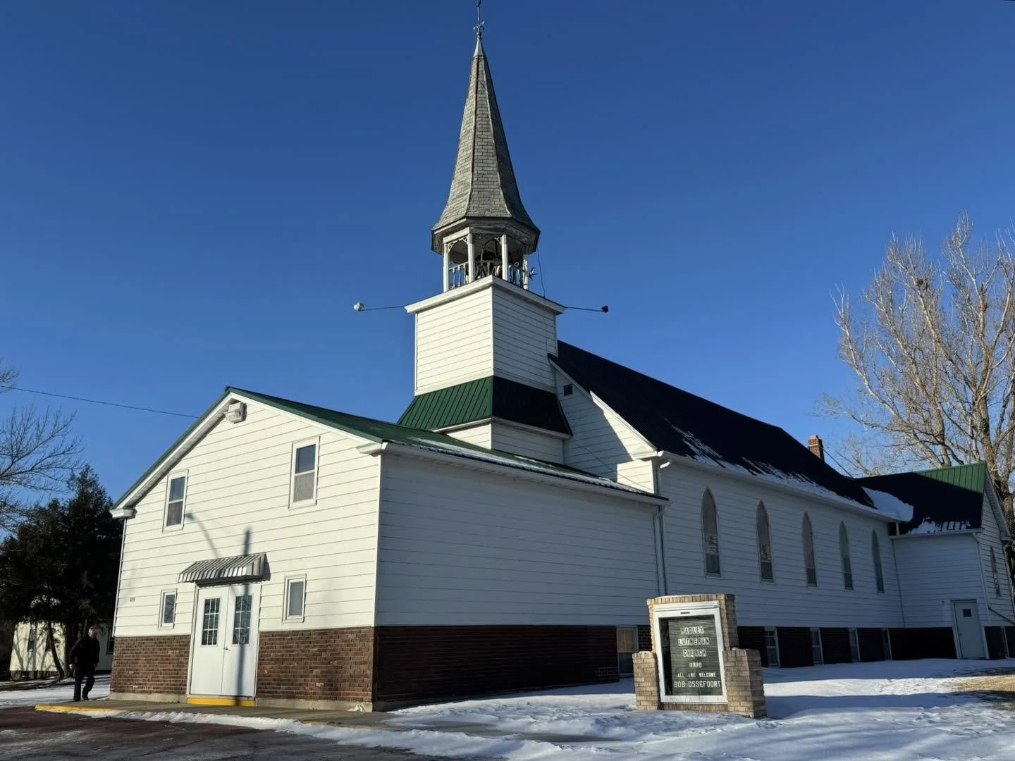 White wooden church with steeple, snow on the ground, and clear blue sky.