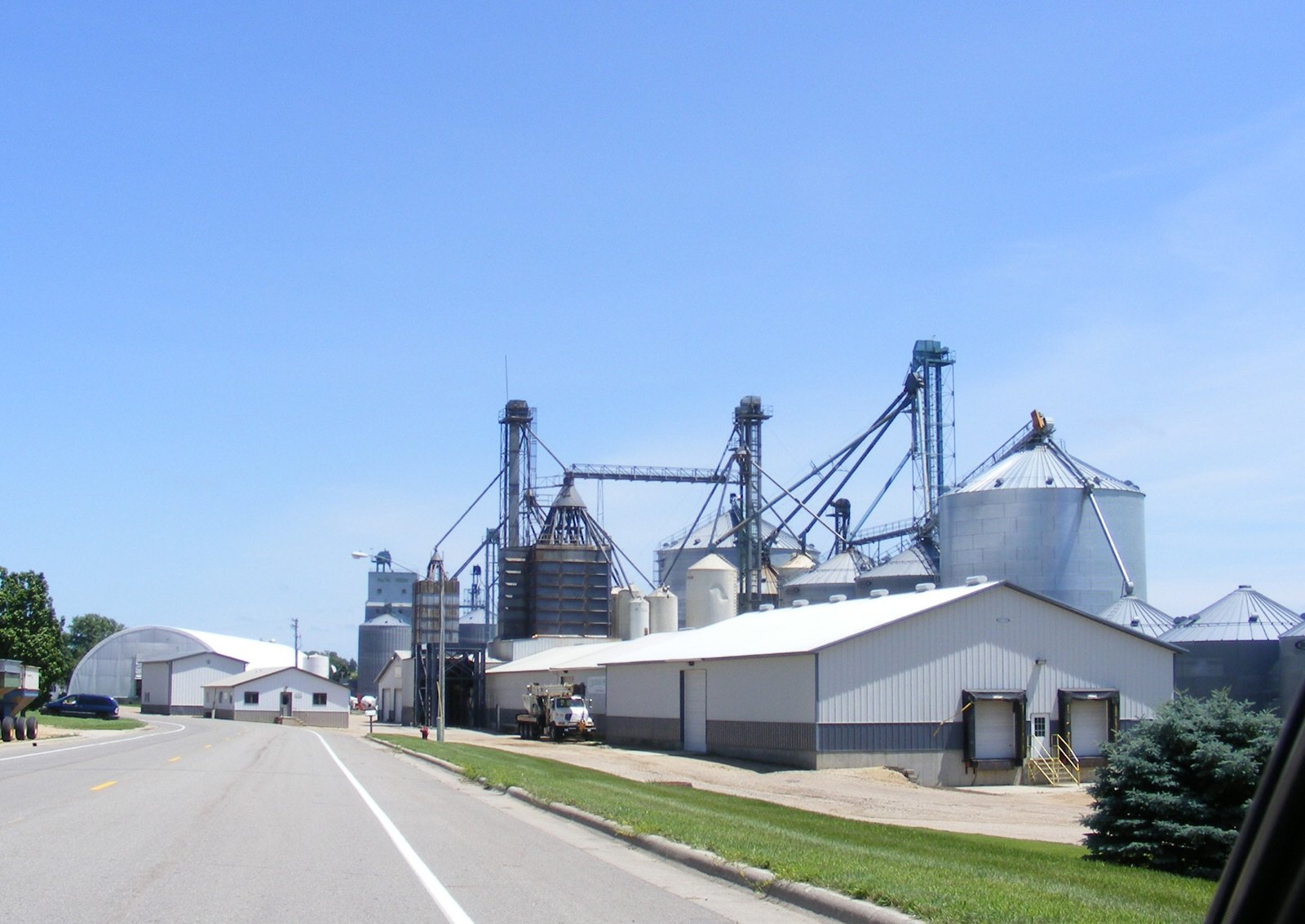 View of a rural industrial farm with silos and storage buildings along a paved road.
