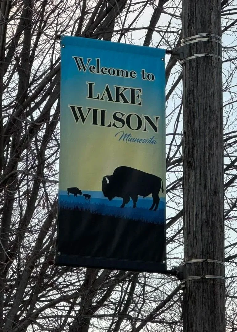 A vertical banner that reads 'Welcome to Lake Wilson Minnesota' with a silhouette of a bison and two smaller animals, likely deer or calves, standing on grass.
