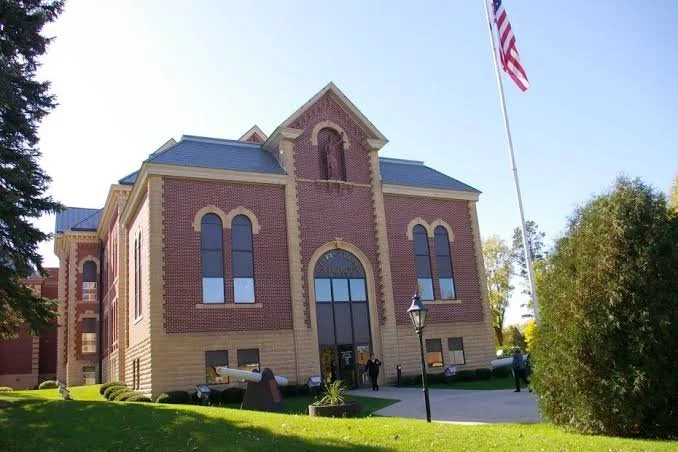 Historic brick courthouse with arched windows, American flag flying, and well-maintained lawn in foreground.