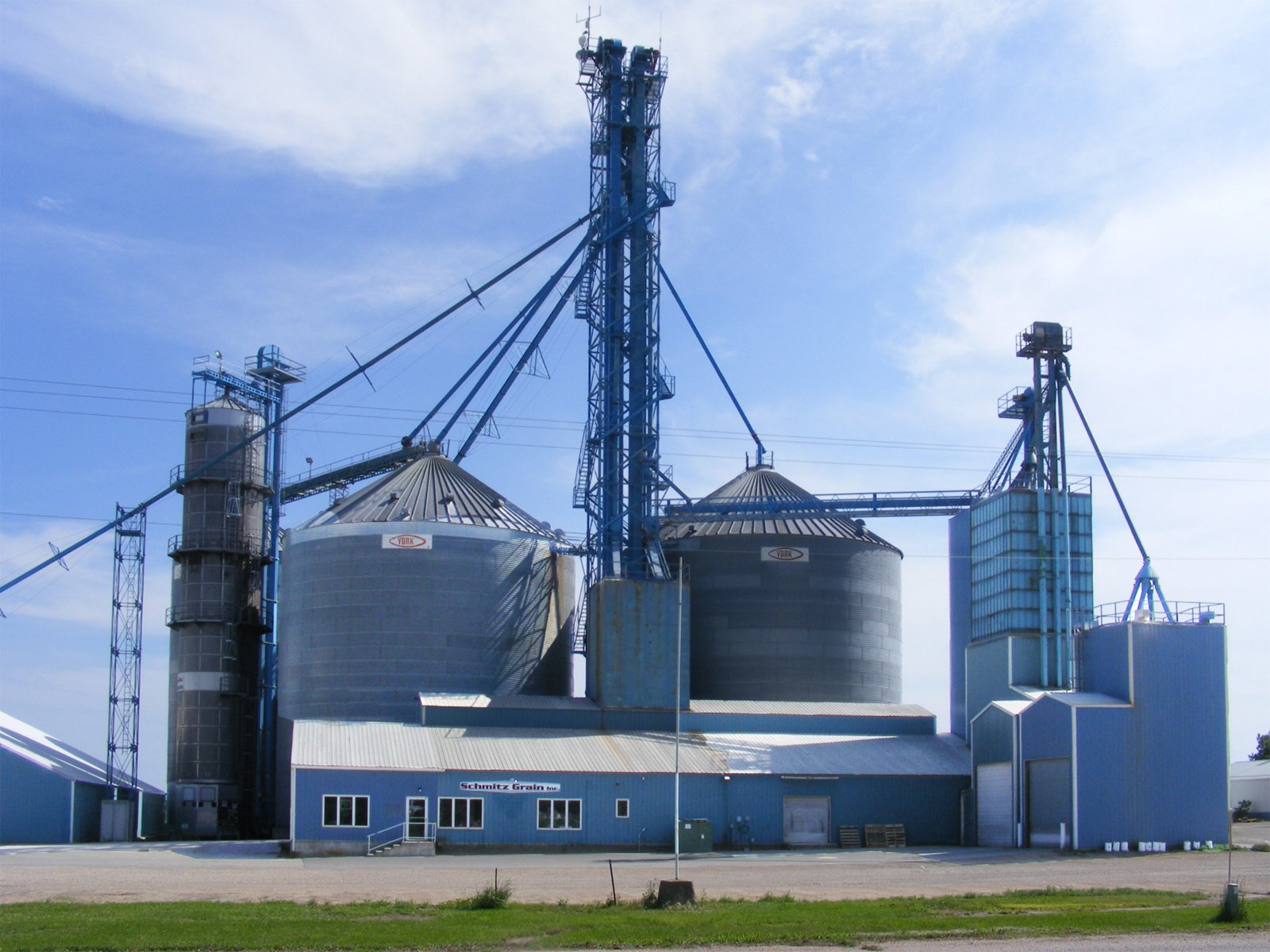An industrial grain storage facility with silos, silos' towers, and supporting structures under a partly cloudy sky.