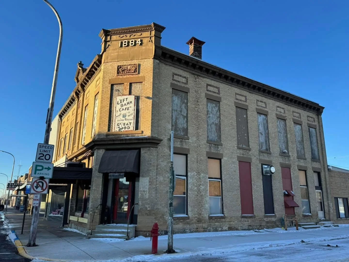 Old brick building with boarded-up windows and a sign for Left Bank Cafe, located at 884, with snow on the ground and a clear blue sky.