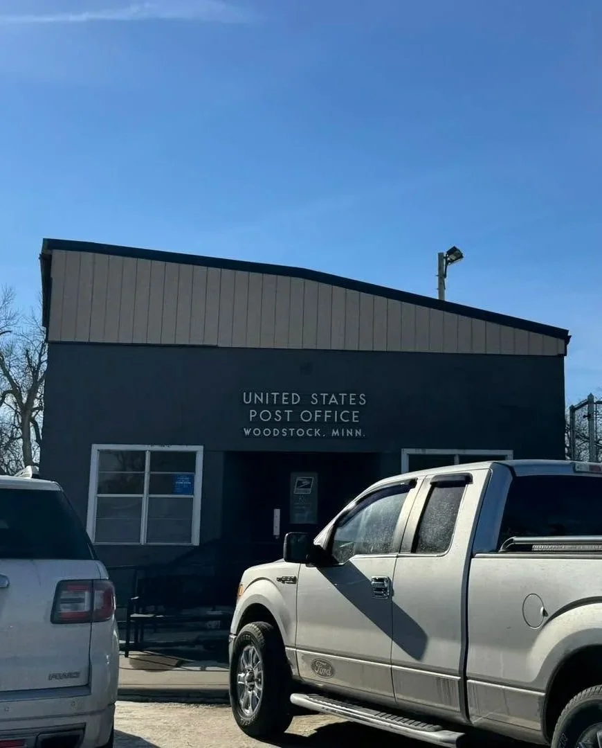 United States Post Office building in Woodstock, Minnesota with parked cars in front.