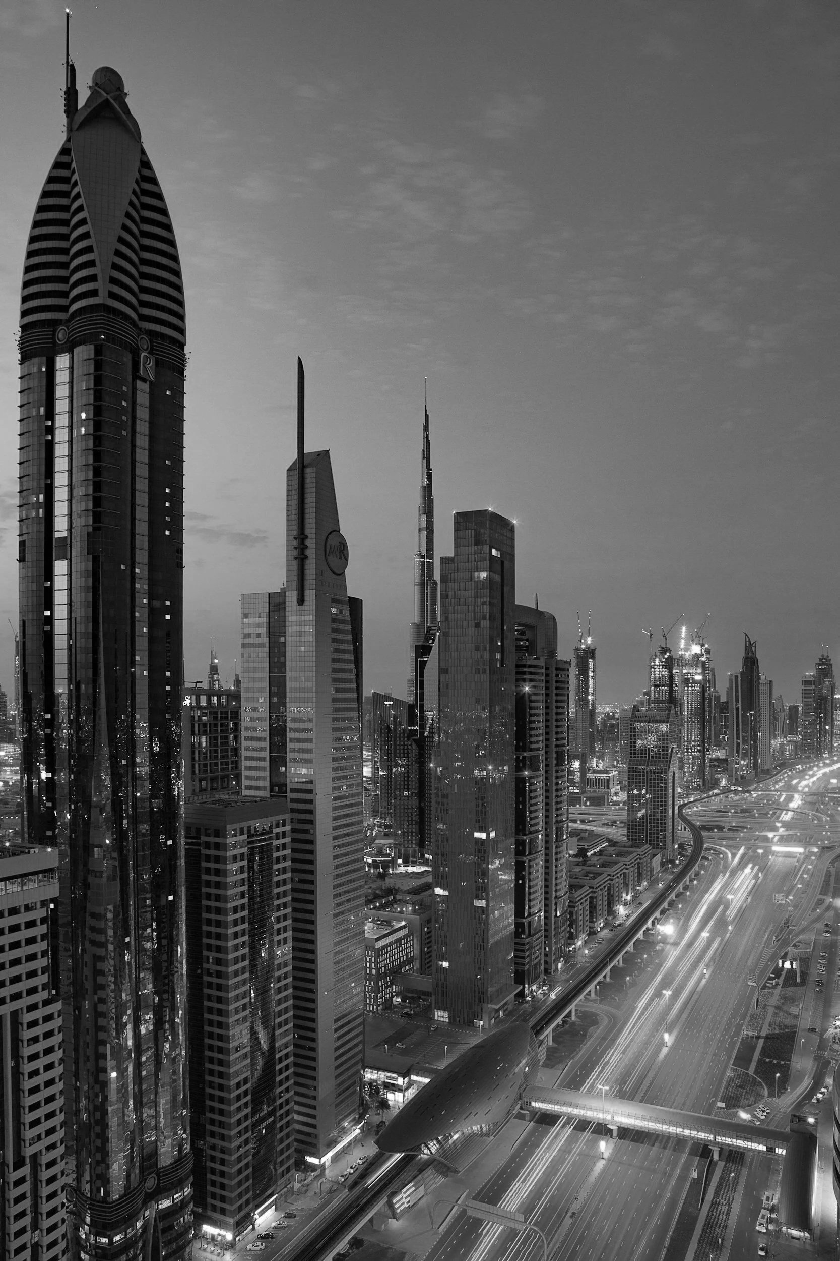 A nighttime view of a city skyline with tall skyscrapers, including the Burj Khalifa, and illuminated roads below.