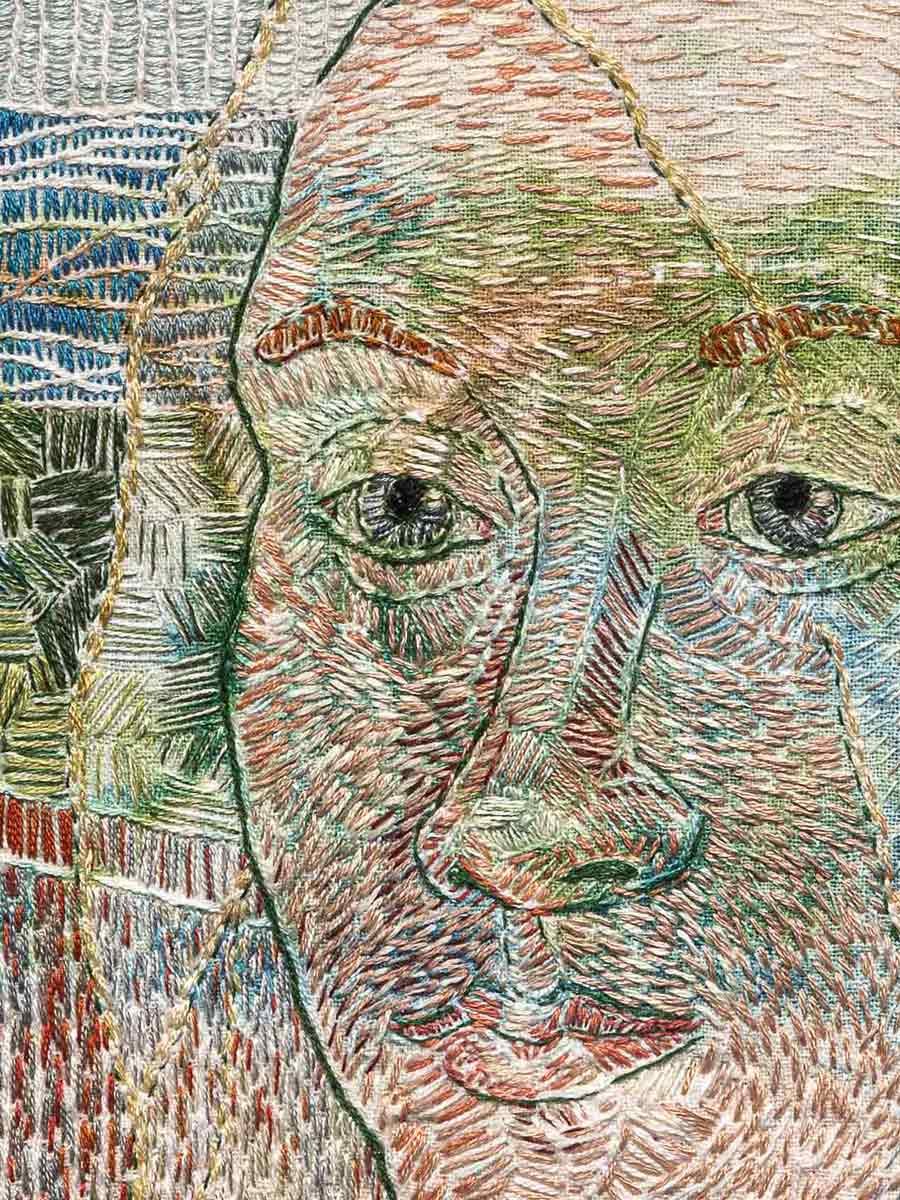 Close-up embroidery of a person's face with detailed stitching and varied thread colors, including parts of plants in the background.