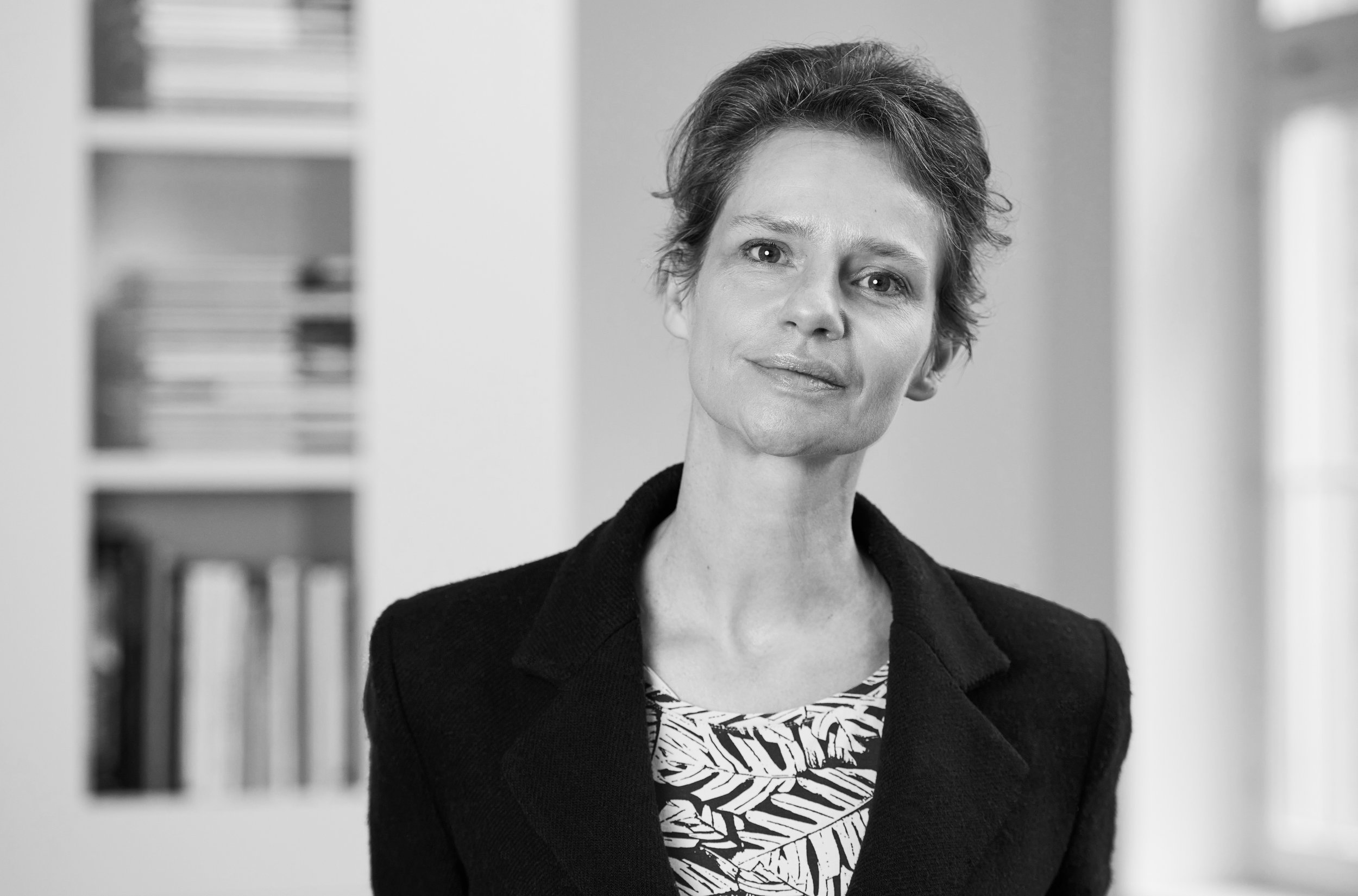 Architektin Sandra Düsterhus, Gründerin und Partnerin bei POINT. Architektur sowie Mitglied des BDA Hessen, in einer Schwarz-Weiß-Porträtaufnahme vor einem Bücherregal.
