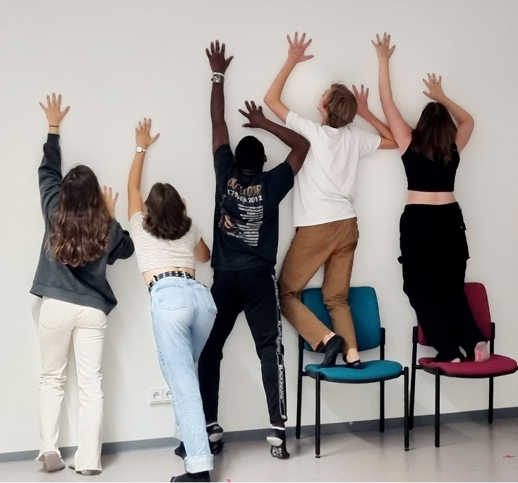 Fünf junge Menschen bei einem Workshop im English Theatre Frankfurt, die gemeinsam vor einer weißen Wand posieren und spielerische Körperhaltungen einnehmen.