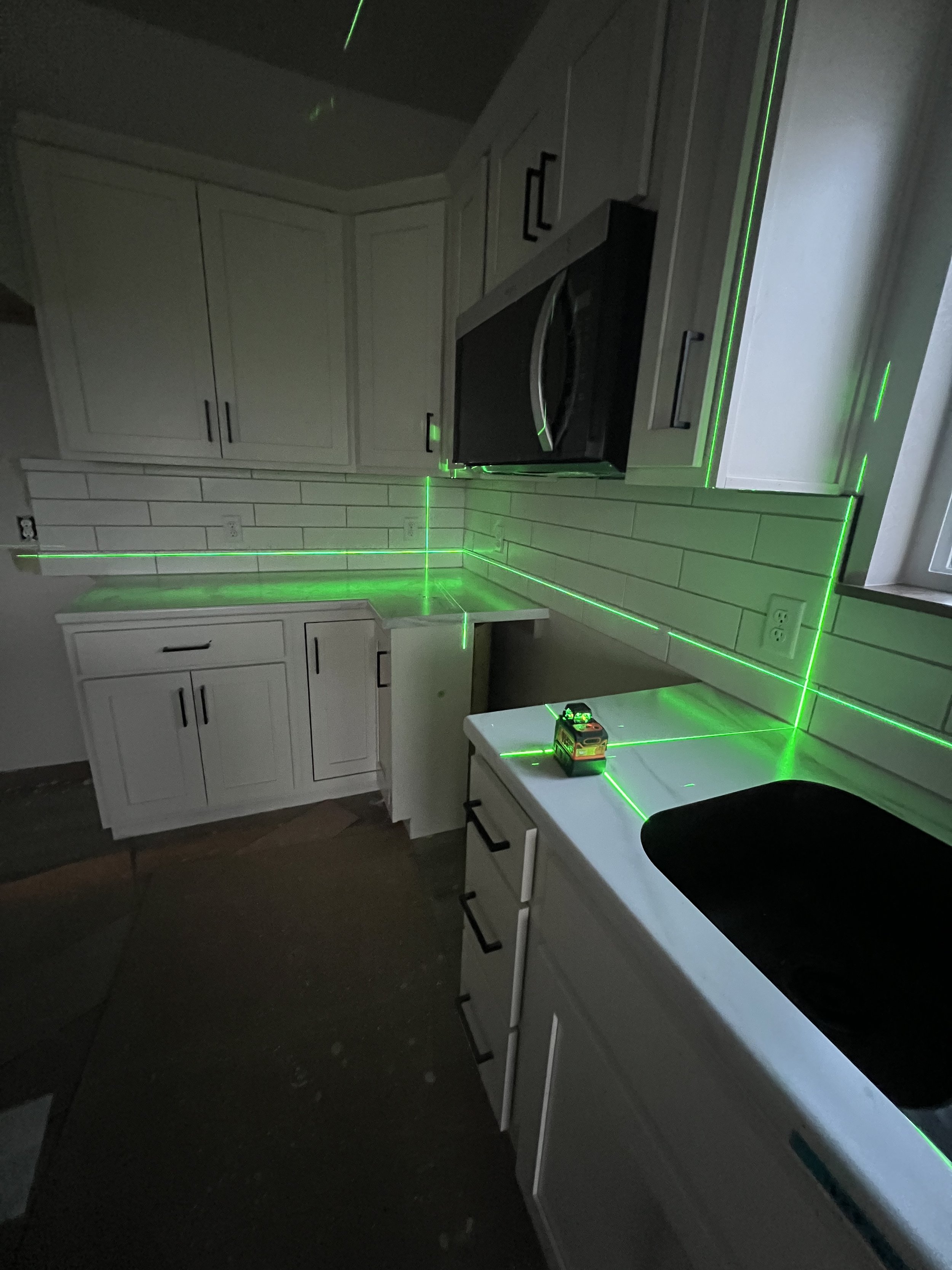Kitchen scene with white cabinets, a microwave, white countertop, and green laser light beams crossing the room.