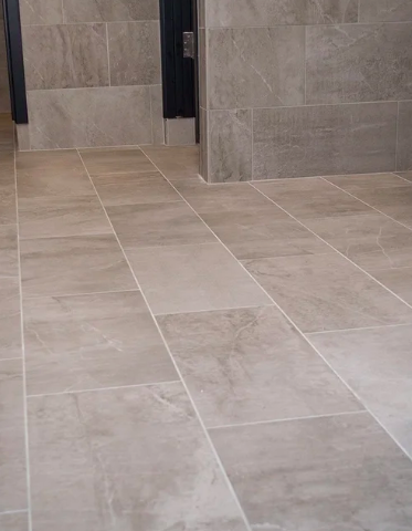 Indoor bathroom with beige tiled floor and gray tiled walls, showing a black door.