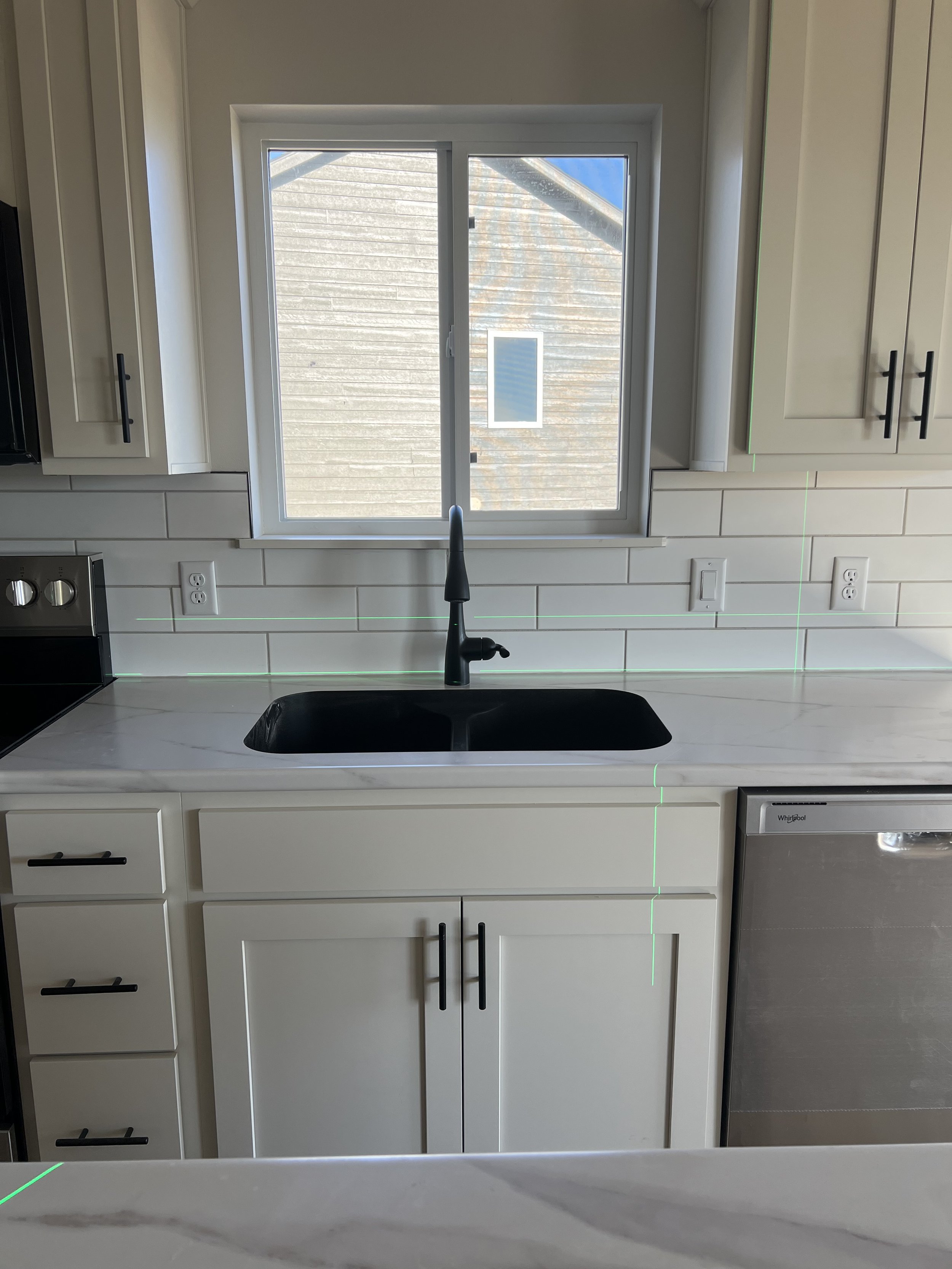 Kitchen with white cabinets, black sink, window above, and stainless steel dishwasher.