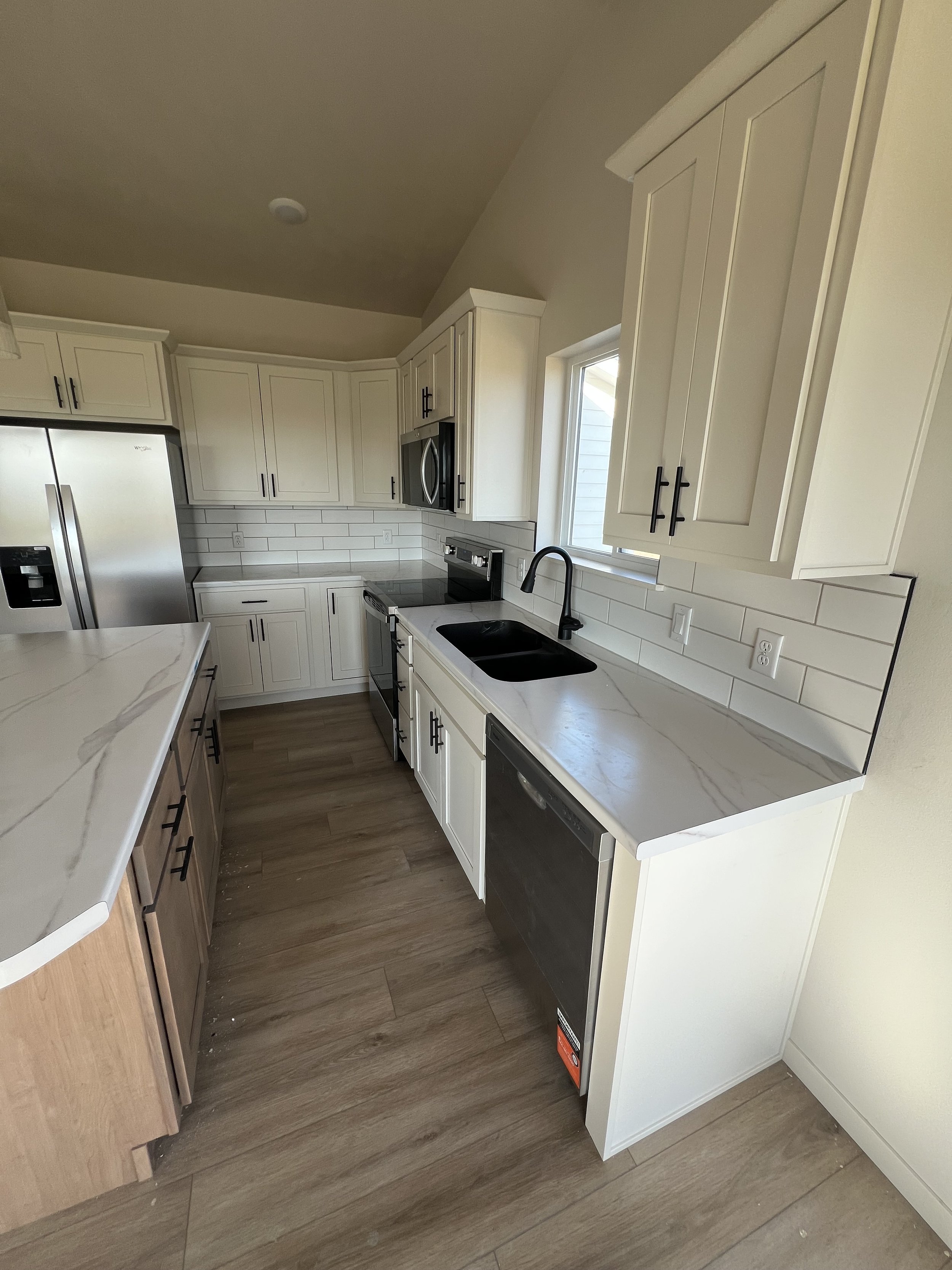 Modern kitchen with white and wood cabinets, a black sink, stainless steel appliances, and hardwood flooring.