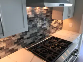 Close-up of a modern kitchen countertop with a built-in stainless steel gas stove and gray tile backsplash.
