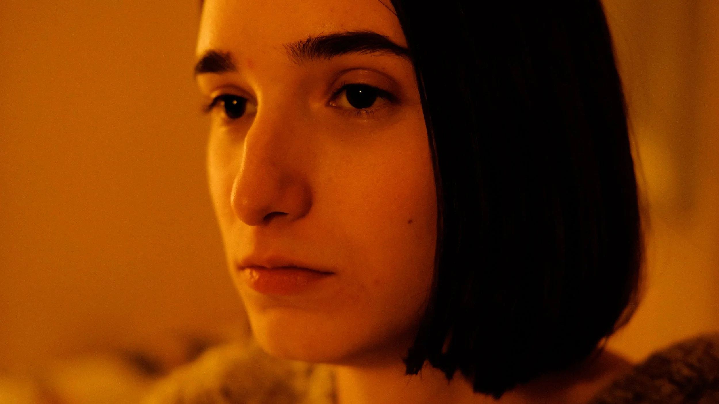 Close-up of a young woman's face with dark hair, looking to the side, in warm lighting.