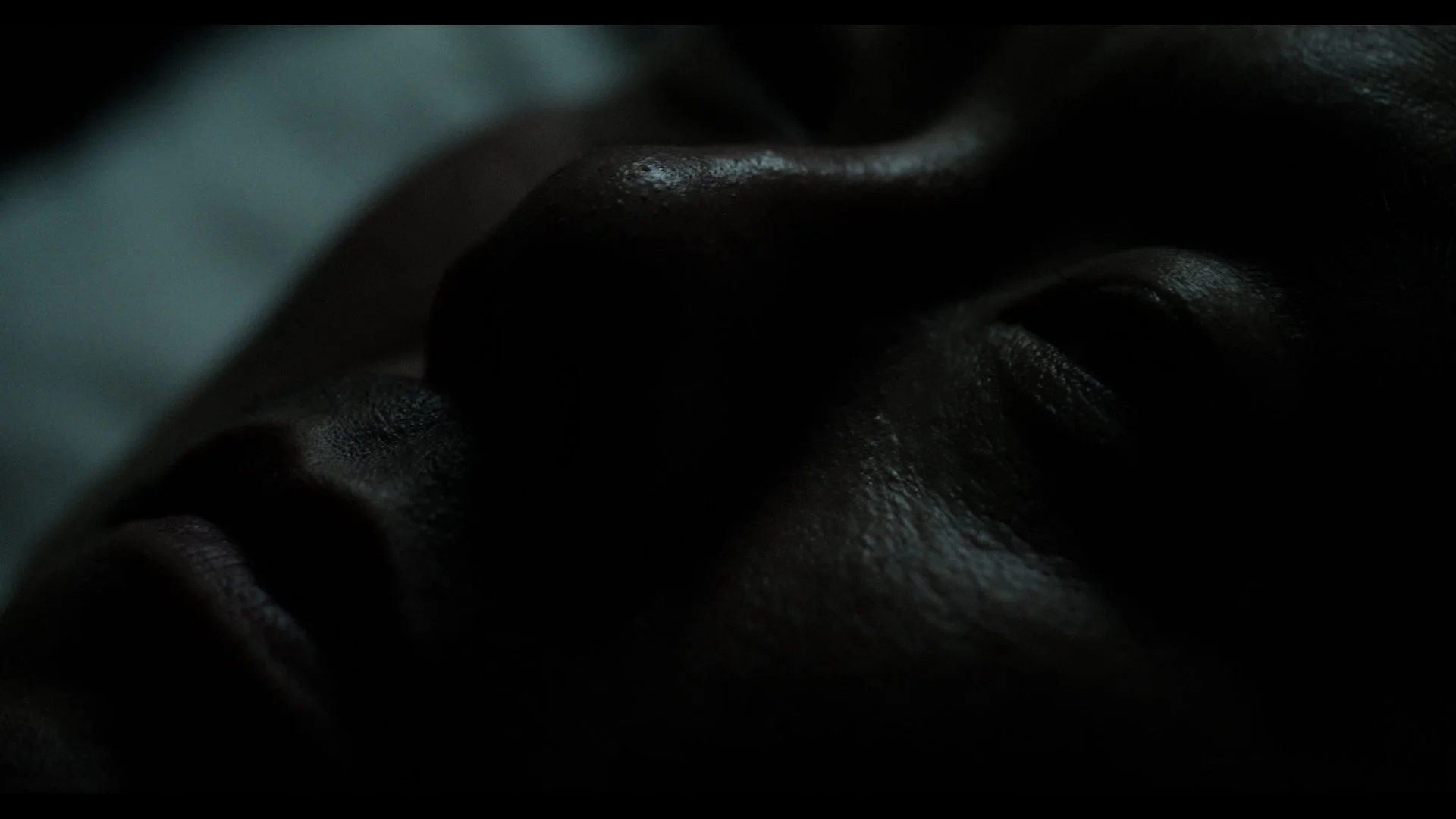 Close-up dark photo of textured skin, possibly a human face or hand, in a shadowy setting.
