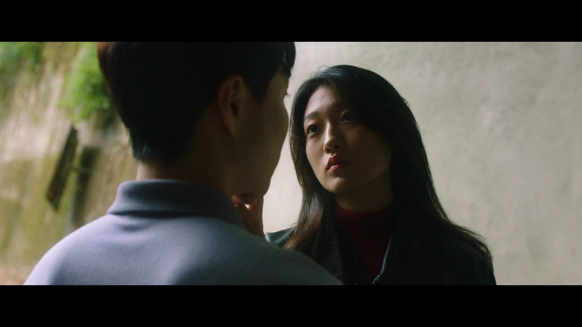 A man and woman face each other closely, with the man's back to the camera and the woman's face visible, in an intimate or tense moment.