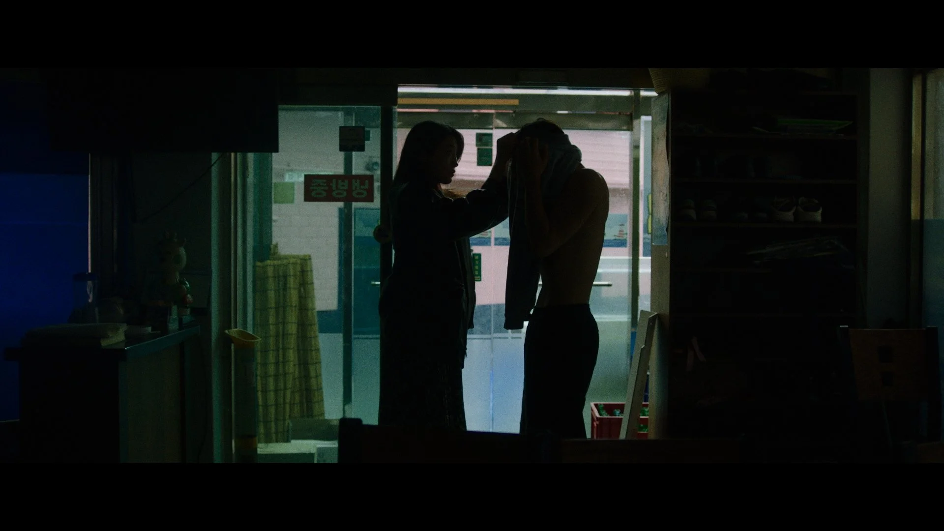 A silhouette of a woman assisting a man in a laundromat, with a glass door and shoe shelves in the background.