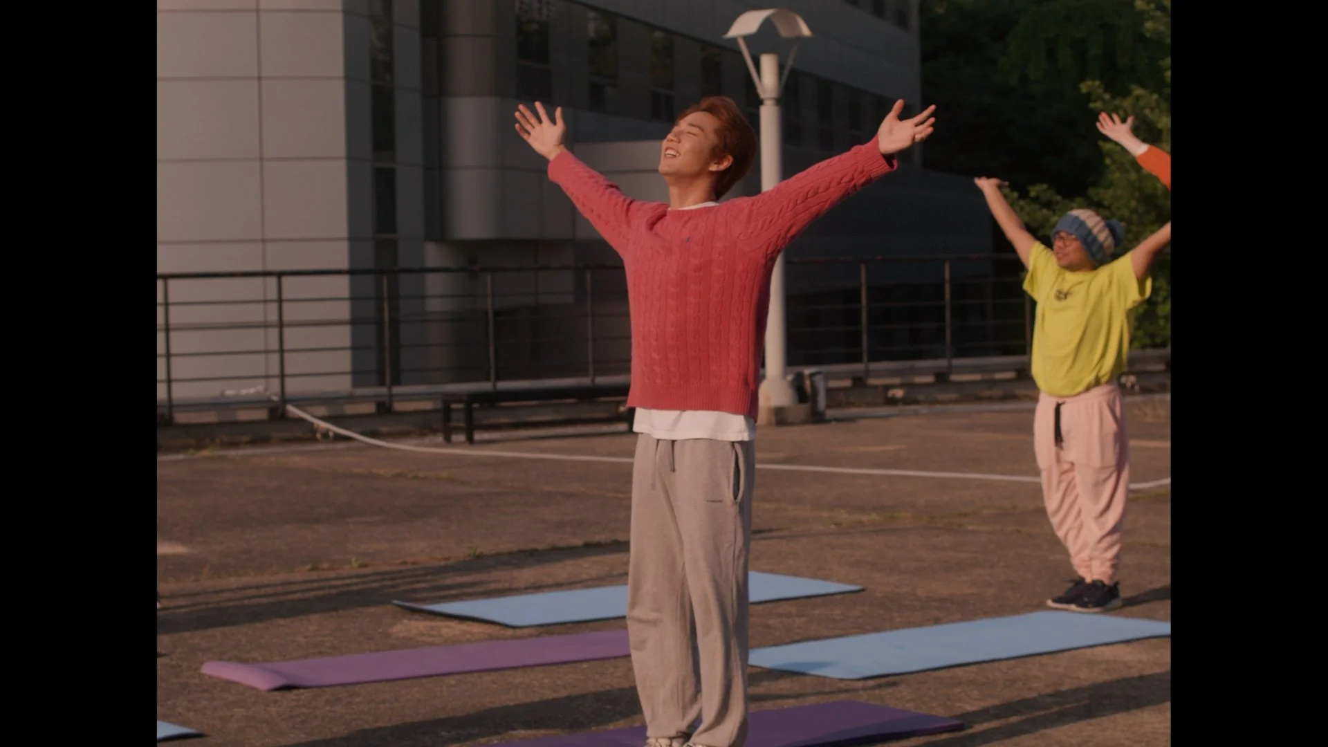 People practicing outdoor yoga or meditation during sunset, with their arms raised and eyes closed, on yoga mats.