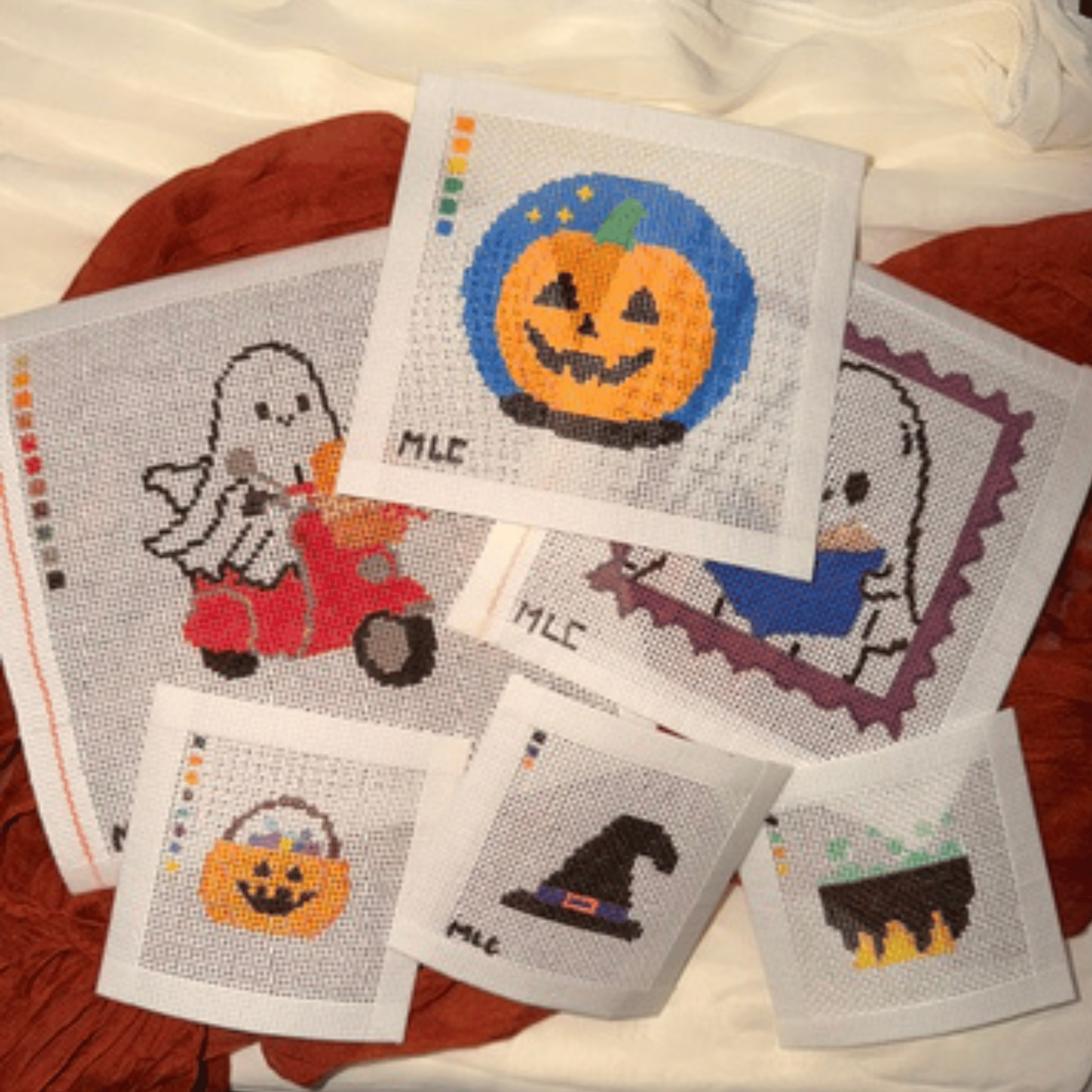 Needlepoint Canvases featuring Halloween-themed images such as a pumpkin with a carved face, a ghost, and a black cat, on white fabric.