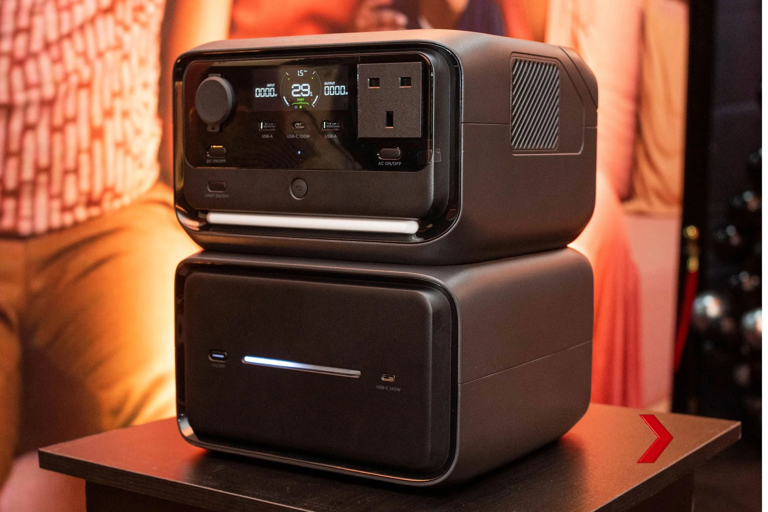 A portable power station with digital display and various ports on a black surface against a warm-colored background.