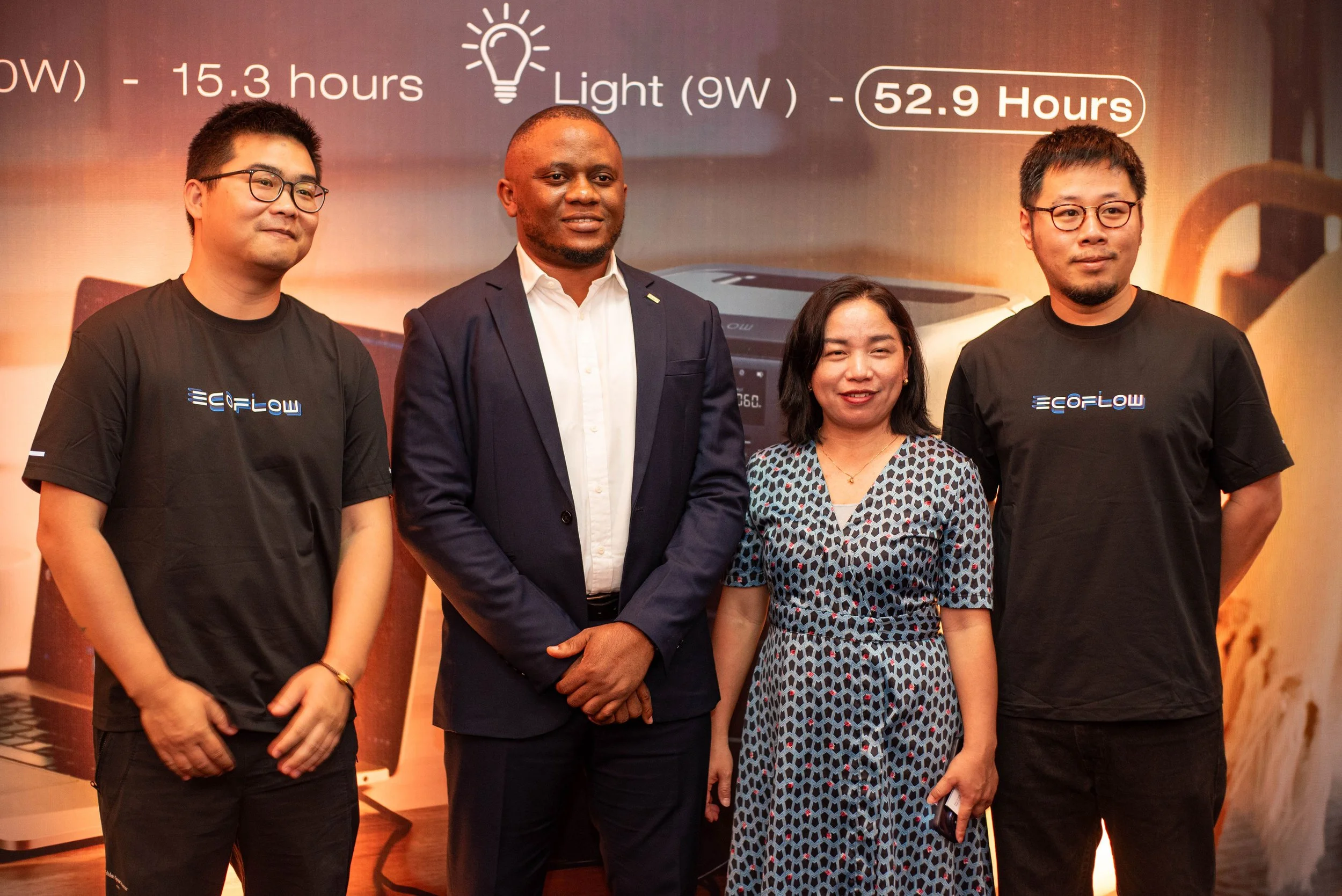Group photo of four people standing indoors, with a large display behind them showing energy consumption statistics.