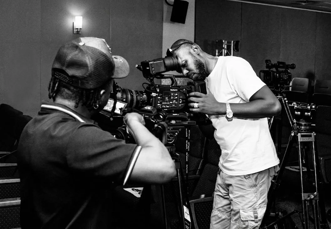 Sane House Media crew members operating professional cinema video cameras. One is operating a camera while the other looks through a monitor, both focused on filming.