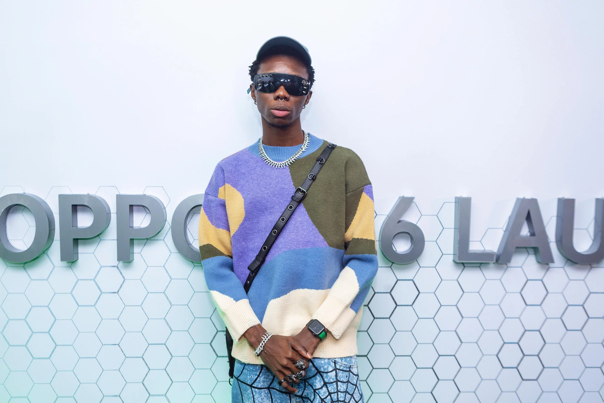 Nigerian musician standing in front of a backdrop with hexagonal patterns and partial large letters.