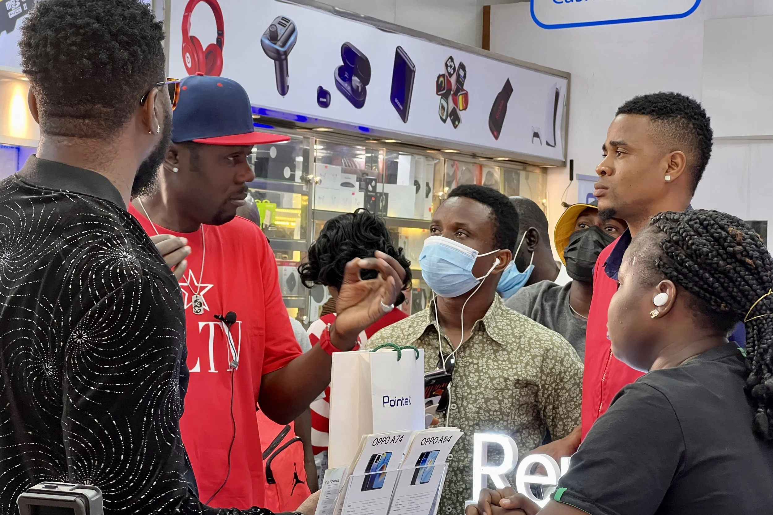 Sane House Media director speaking to cast and crew during a video shoot at a tech store, with phone and accessory displays in the background.