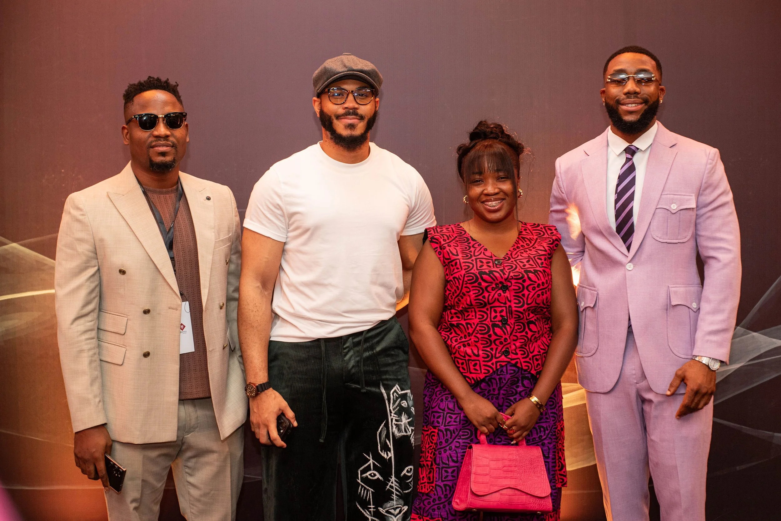 A group of five people standing side by side against a plain background, dressed in stylish clothing, smiling and posing for the camera.
