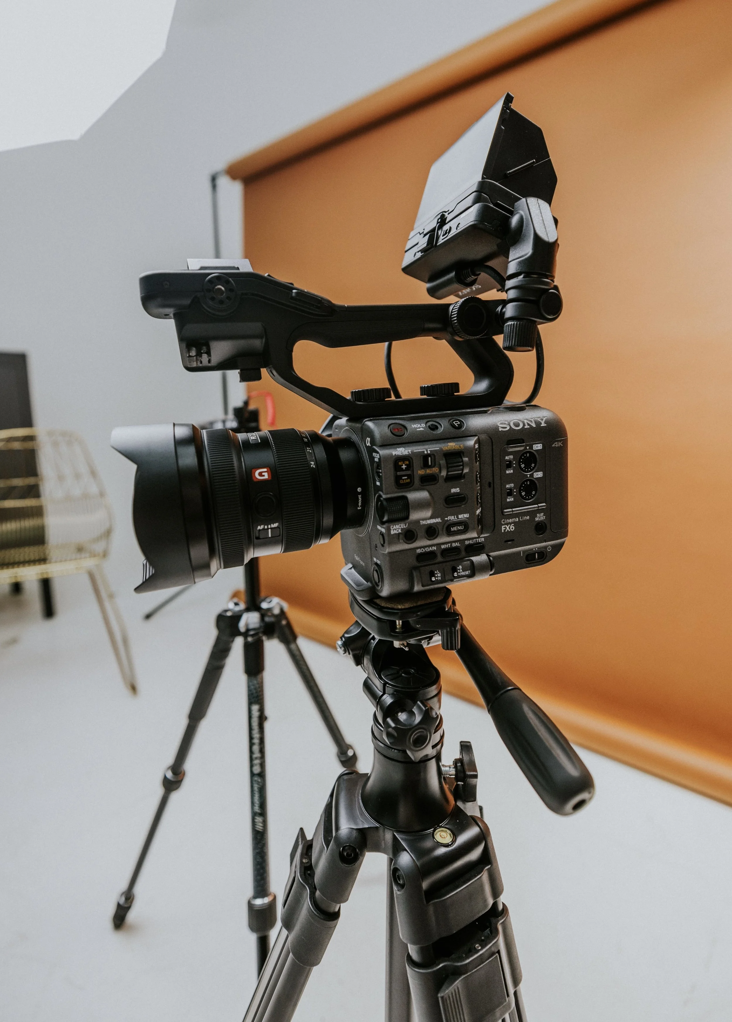 Professional video camera on a tripod in a studio with a brown backdrop.