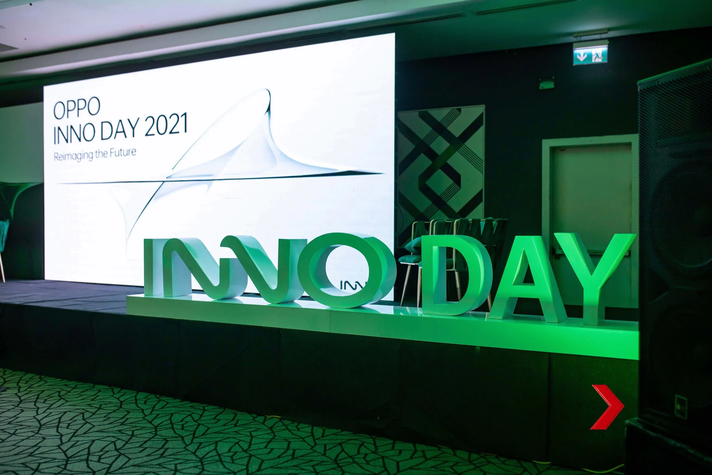 Large digital screen displaying 'OPPO INNO DAY 2021 Reimagining the Future' at a corporate event, with green illuminated 3D letters spelling 'INNOVATION' on a stage in front.