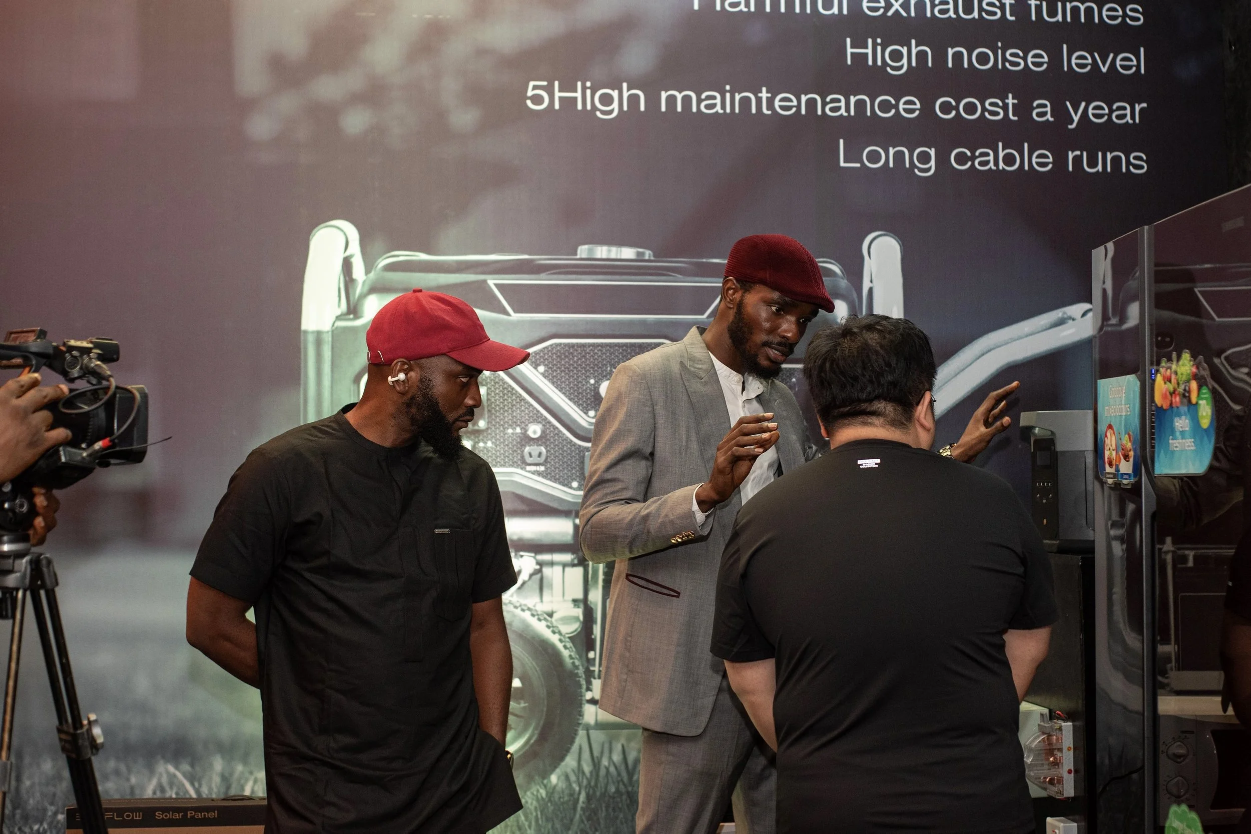 Group of men engaged in a discussion at an event, with a large poster in the background displaying information about exhaust fumes and maintenance costs.
