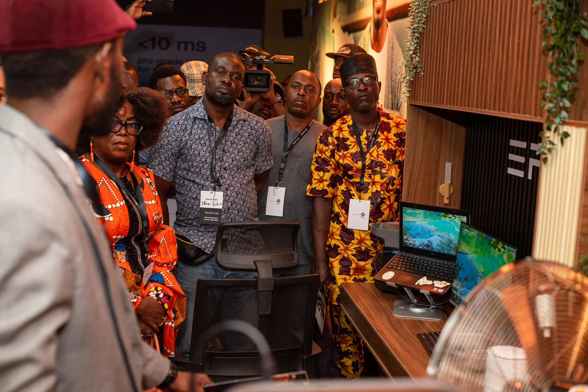 Group of diverse people standing around a table with laptops and monitors at an EcoFlow event, engaging with displays and technology.
