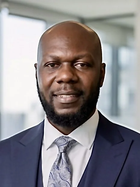 Professional man in a suit and tie posing in an office with large windows.