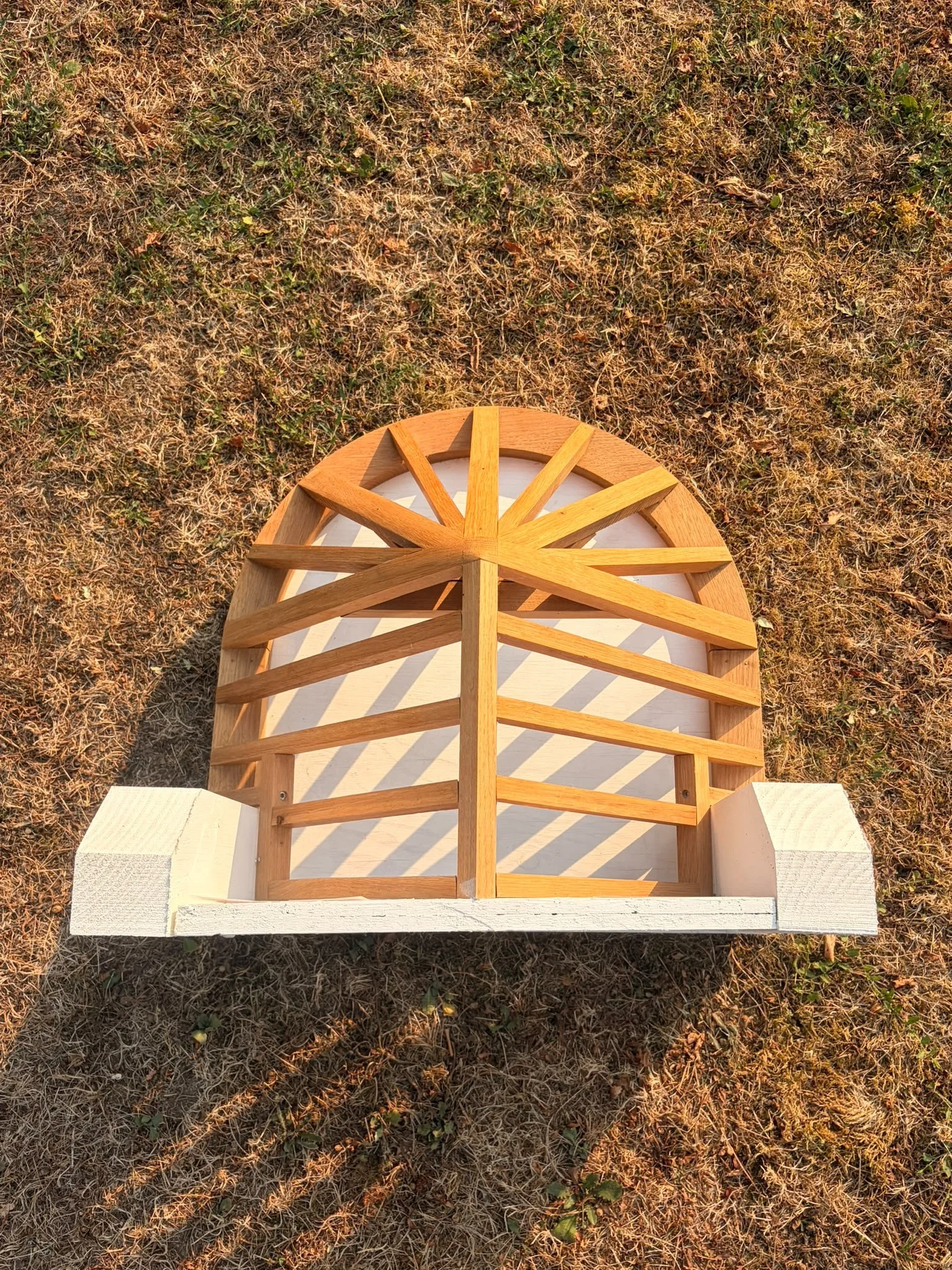 Une structure en bois sur un sol de terre sèche avec des herbes jaunies et quelques petites plantes vertes.