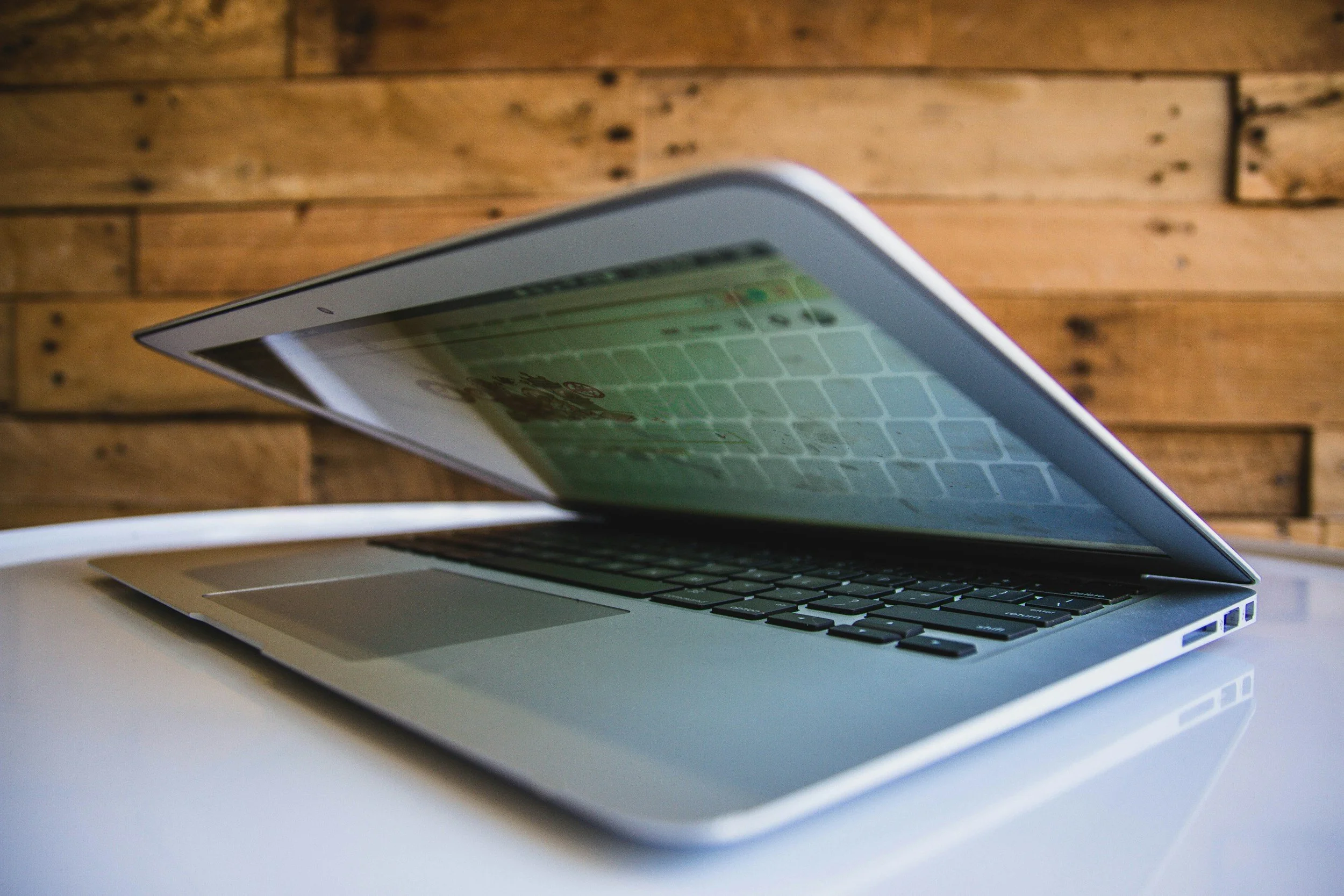 A silver laptop with a black keyboard sitting on a white surface, opened and displaying a colorful screen, against a wooden wall background.
