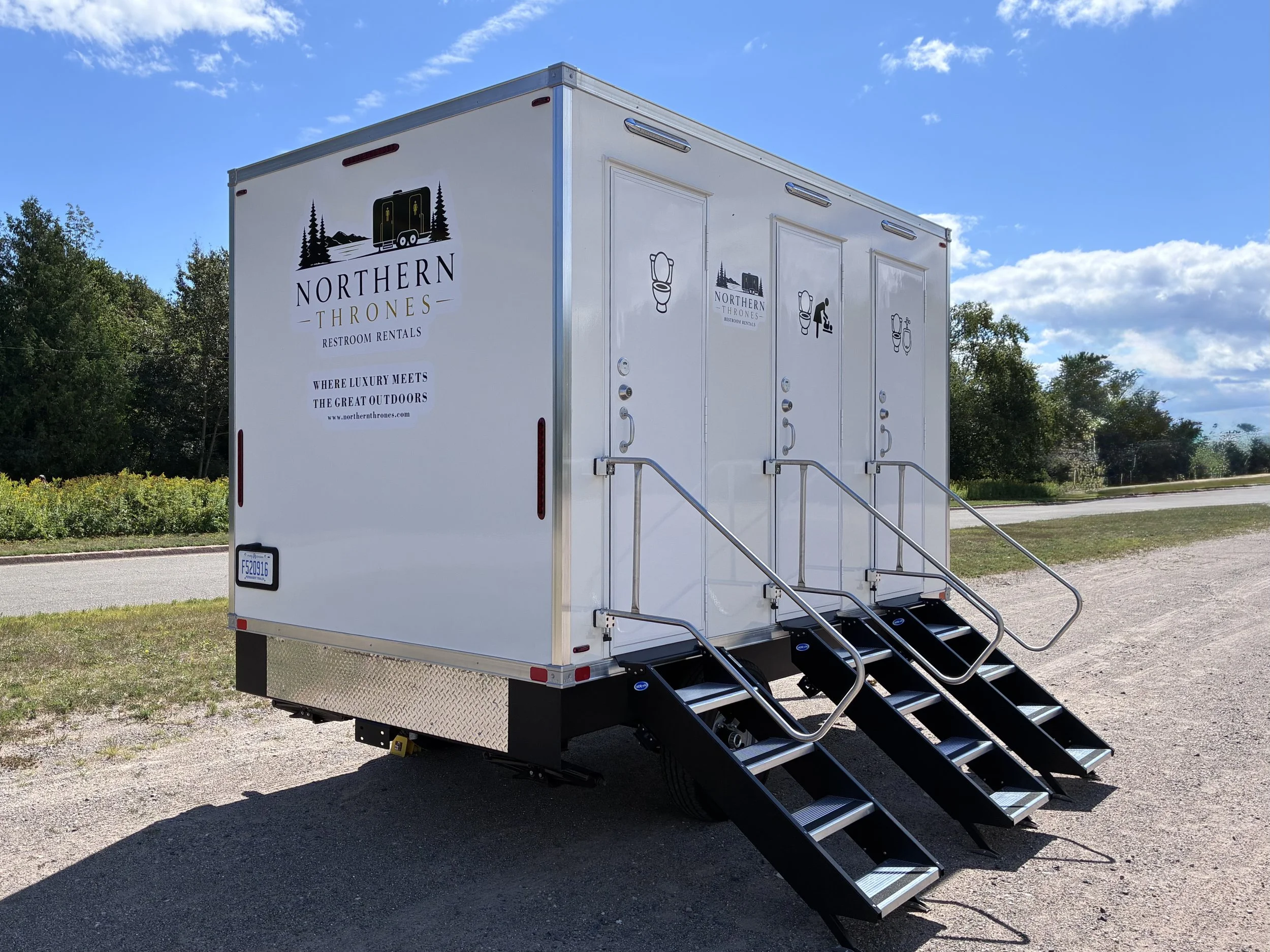 Rear view of a Northern Thrones Restroom Rental Trailer featuring safety railings, and door graphics for indicating toilet, baby changing table and urinal.